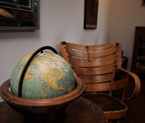 An antique global sits on a round table next to a wooden chair.
