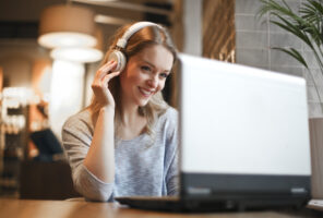 Woman with headphones smiling while looking at a laptop in a cozy, softly lit room, immersed in automated accessibility testing.