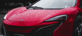 A red sports car with raindrops on its surface is parked outdoors.