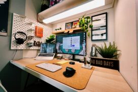 A neatly organized home office desk with a laptop, monitor, keyboard, mouse, plants, headphones, and a sign that reads "NO BAD DAYS.