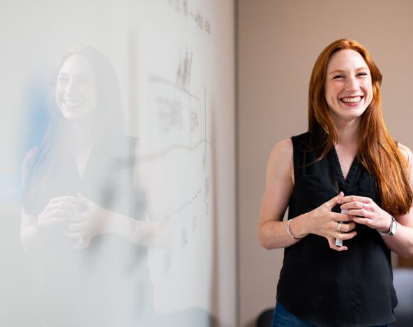 An agile tester woman smiling in front of a whiteboard.
