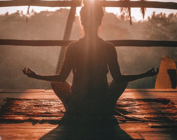 An agile tester meditating on a wooden deck with palm trees in the background.