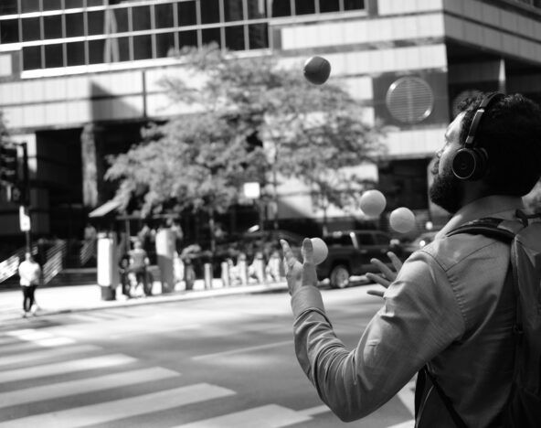 An agile man juggling balls in the middle of the street.