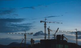 Construction cranes silhouetted against the sky at dusk.