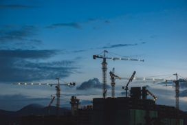 Construction cranes silhouetted against the sky at dusk.