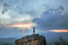 A man standing on top of a rock with his arms outstretched.