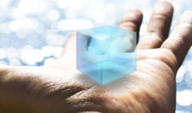 Against the backdrop of a sparkling lake, an outstretched palm holds a blue, virtual cube.