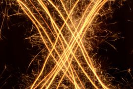 Over a black background, golden light streaks in the pattern of an "X" inscribed in a circle