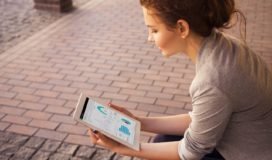 Outside on a brick patio, a young woman studies a dashboard on a tablet