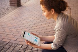 Outside on a brick patio, a young woman studies a dashboard on a tablet