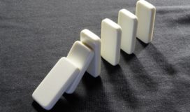 White dominoes on a dark gray cloth beginning to fall over