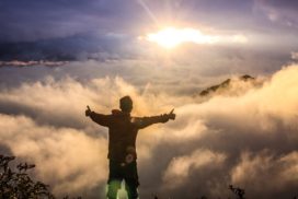man looking down on clouds standing on a mountain with his thumbs up