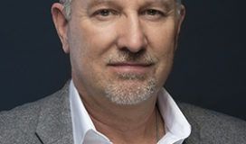 A man in a gray suit and white shirt is posing for a photo.