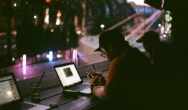 At the window in a darkened coffee shop, people work on laptops.