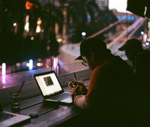 At the window in a darkened coffee shop, people work on laptops.