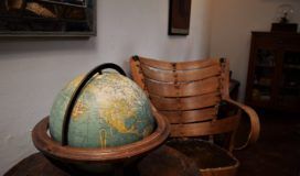 An antique global sits on a round table next to a wooden chair.
