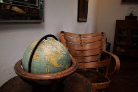 An antique global sits on a round table next to a wooden chair.