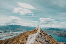 A person standing on top of a mountain overlooking Lake Wanaka in awe.