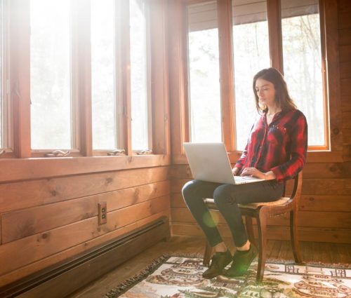 A woman performing automation testing tasks while sitting on a chair in front of a window with her laptop.