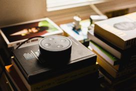 An echo dot, equipped with Alexa skills, sitting on top of a stack of books.