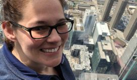 A smiling woman taking a selfie with skyscrapers.