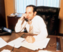 A middle aged man sitting at a desk talking on the phone.