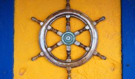 A wooden ship wheel on a blue wall.