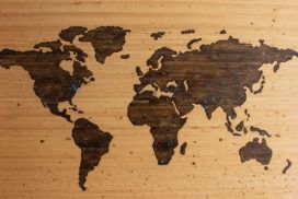 A wooden world map with blue pins on it.