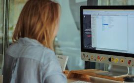 A woman is sitting at a desk using Angular Material to design and enhance the interface on her computer screen.