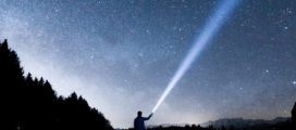 A person holding a flashlight under a starry sky.