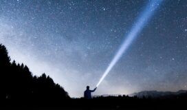 A person holding a flashlight under a starry sky.