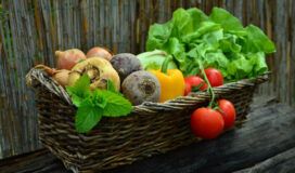 A wicker basket full of vegetables on a wooden table.