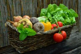 A wicker basket full of vegetables on a wooden table.