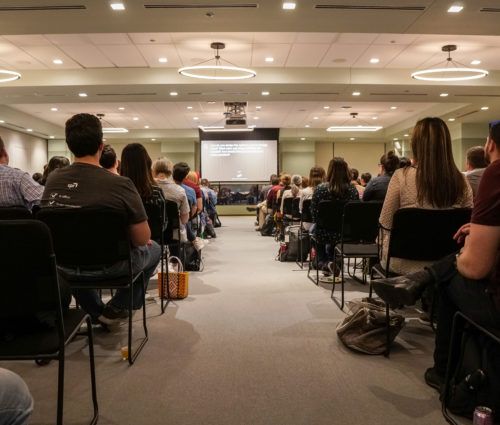 Low angle view of people watching a presentation in a brightly lit room.