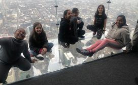 A group of kids posing on the glass floor of a skyscraper.