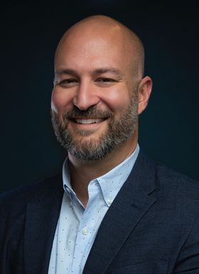 A bald man smiling in front of a blue background.