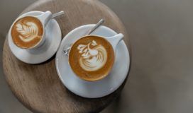 Two agile latte art cups on a wooden table.