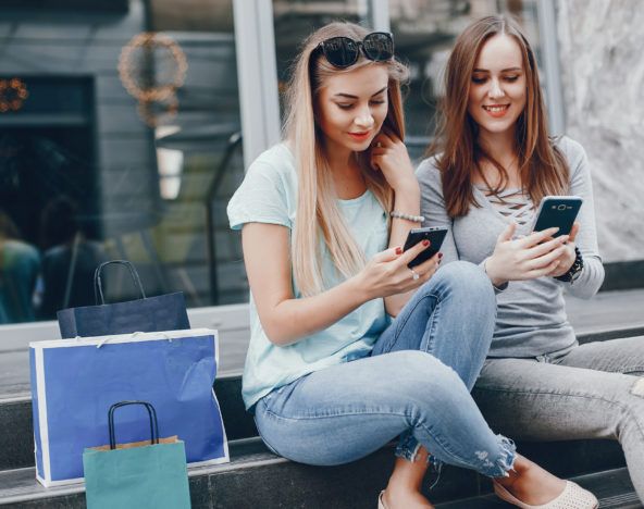 Two women sitting on steps browsing their phones with high-capacity data access.