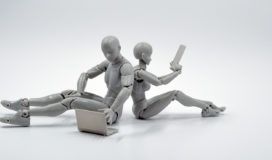 Two mannequins utilizing AutoML, sitting on the ground and holding a laptop.