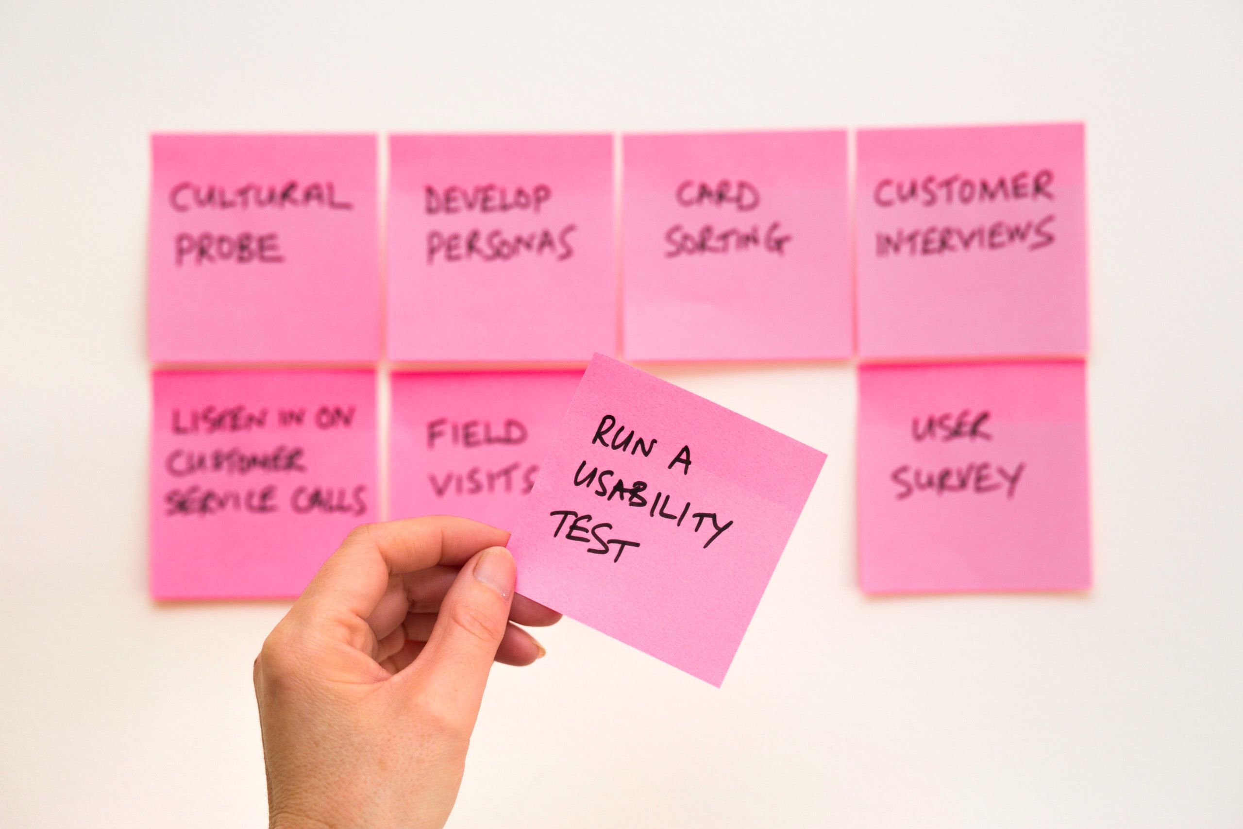 A person holding up pink post it notes with the words run a usability test.