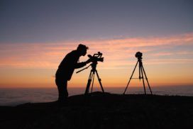 A silhouette of a man with a camera and tripod on top of a mountain.
