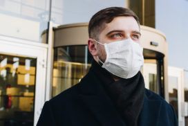 A persona wearing a surgical mask in front of a building.