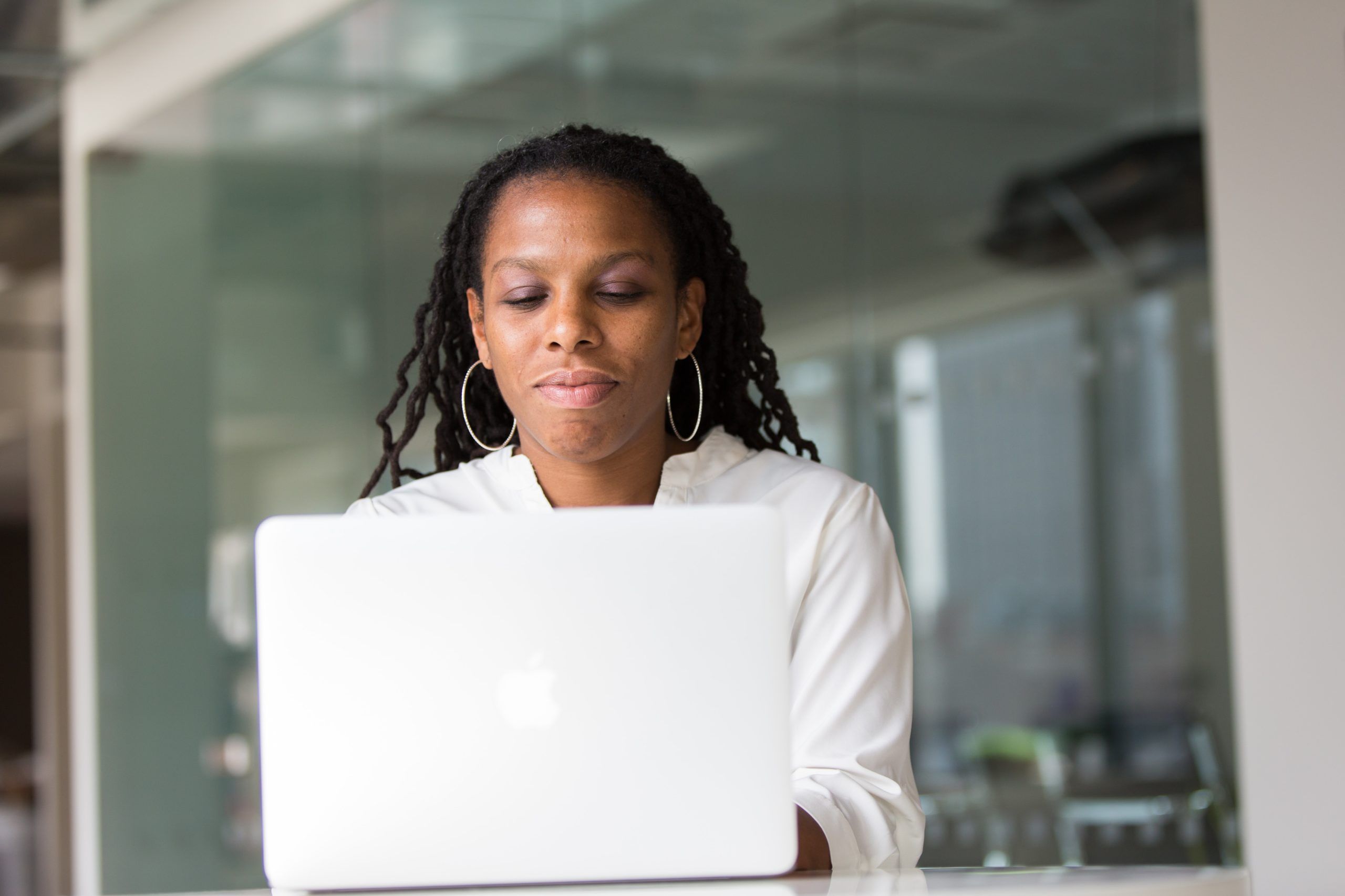 A black woman working on a laptop in an office, utilizing the cloud for seamless collaboration and data storage.