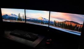 Three monitors are set up in a dark room to support a cloud strategy.