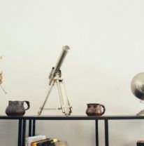 A shelf with books, vases, and a telescope.