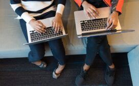 Two women, engaged in the history of technology, sitting on a couch with laptops.