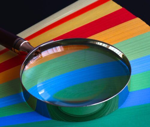 A magnifying glass testing a stack of colored paper.