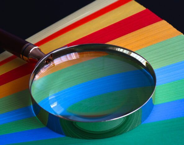 A magnifying glass testing a stack of colored paper.