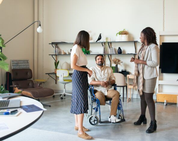 A group of people **interacting** in an office with a person in a wheelchair.
