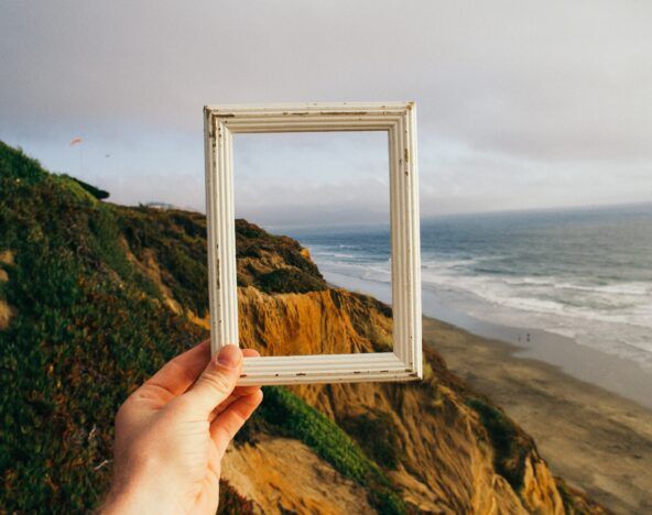 A person sharing knowledge, holding up a picture frame on a cliff overlooking the ocean.